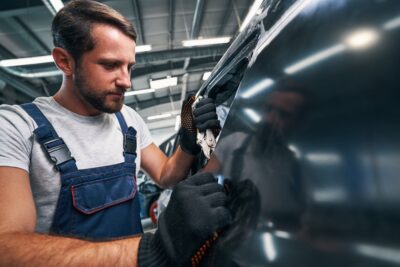 An individual services a car at an auto body shop.